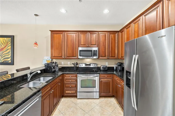 Kitchen featuring stainless steel appliances, a sink, light tile patterned floors, brown cabinets, and dark stone counters