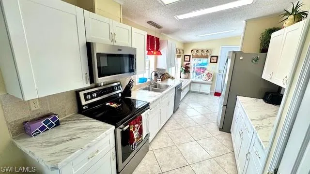 Kitchen with stainless steel appliances, a textured ceiling, white cabinetry, light tile patterned flooring, and hanging light fixtures