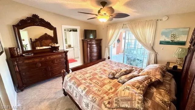 Bedroom with a textured ceiling, light tile patterned floors, ceiling fan, and connected bathroom
