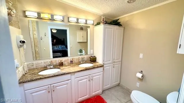 Full bath featuring a textured ceiling, crown molding, ensuite bath, double vanity, and light tile patterned floors