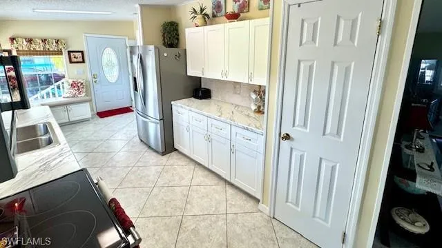 Kitchen with light tile patterned flooring, white cabinetry, range with electric stovetop, a textured ceiling, and stainless steel refrigerator with ice dispenser