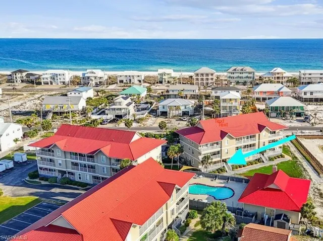 Coastal community with a vibrant blue ocean backdrop, featuring multiple residential structures with red roofs and balconies, and a communal swimming pool