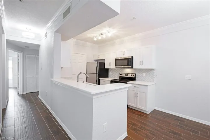 Kitchen featuring kitchen peninsula, white cabinets, dark hardwood / wood-style flooring, appliances with stainless steel finishes, and sink