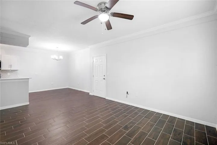Empty room featuring crown molding, dark hardwood / wood-style floors, and ceiling fan with notable chandelier
