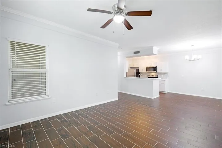 Unfurnished living room featuring ornamental molding, ceiling fan with notable chandelier, and dark hardwood / wood-style flooring