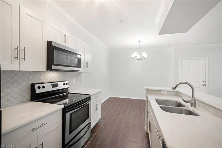 Kitchen with appliances with stainless steel finishes, sink, decorative light fixtures, white cabinets, and dark wood-type flooring
