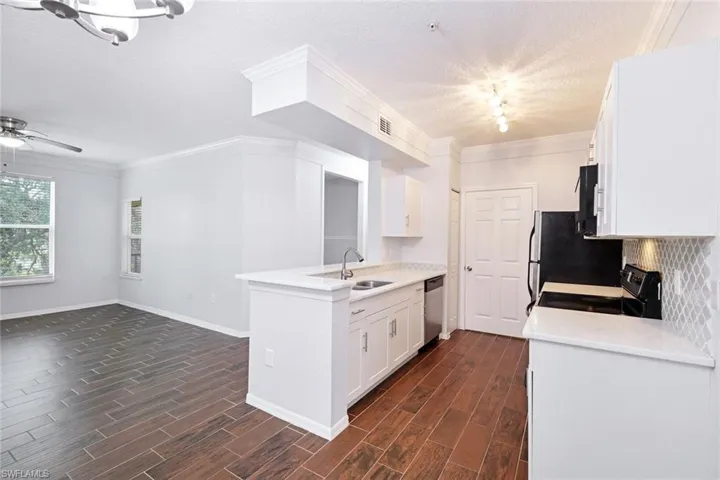 Kitchen with sink, black appliances, white cabinets, and dark wood-type flooring