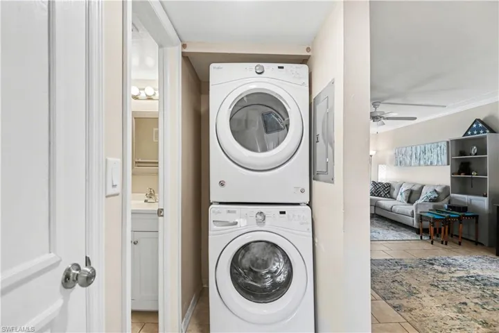 Laundry area with light tile patterned floors, stacked washer and clothes dryer, electric panel, and ceiling fan