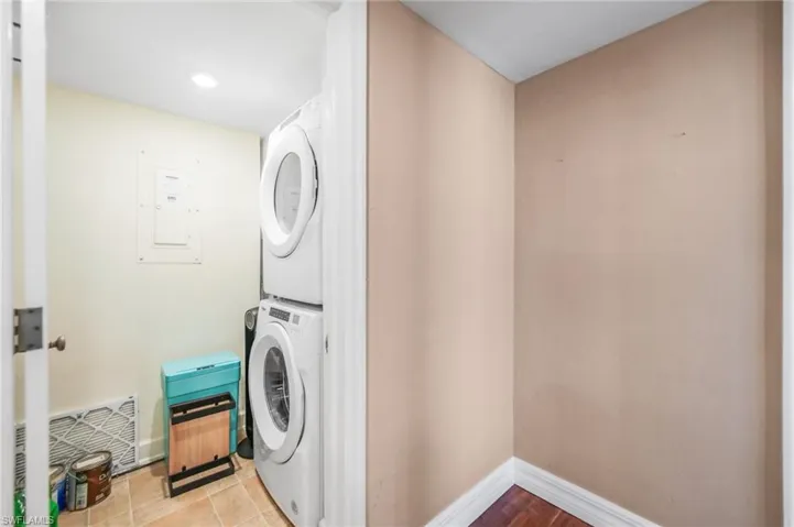 Laundry room featuring electric panel and stacked washer / dryer