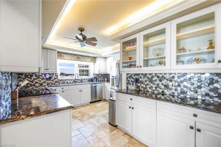 Kitchen with white cabinetry, dark stone countertops, stone tile floors, stainless steel appliances, and a ceiling fan