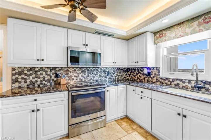 Kitchen with white cabinets, stainless steel appliances, ceiling fan, dark stone countertops, and ornamental molding