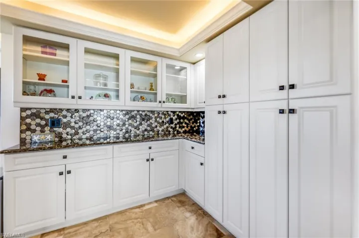 Bar featuring white cabinetry, dark stone countertops, tasteful backsplash, and glass fronted cabinets