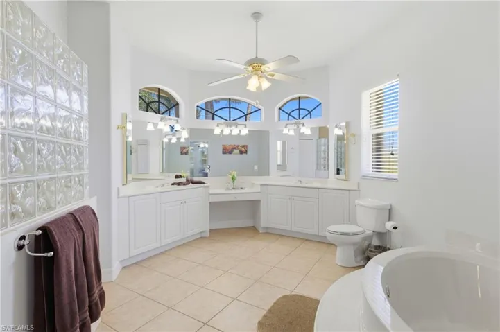 Spacious bathroom featuring tiled flooring, a large soaking tub, a white vanity with double sinks, and a glass block shower wall