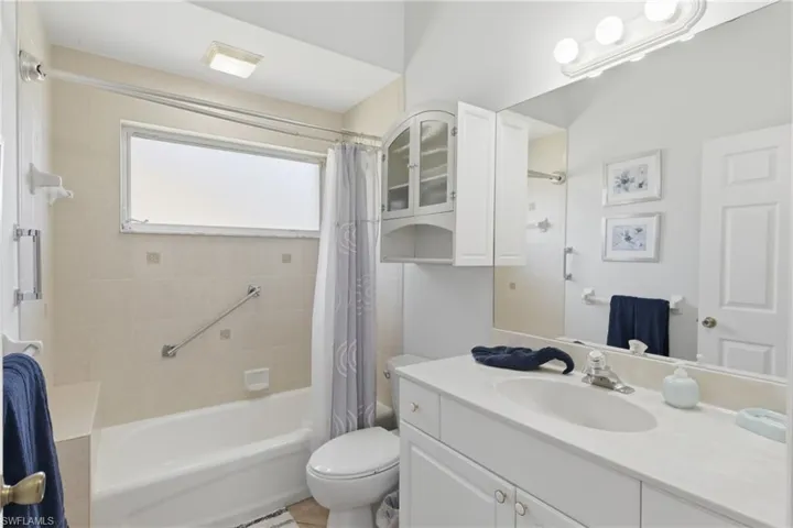 The bathroom features a vanity with a white countertop and an integrated sink, a large mirror, and a bathtub with tiled walls