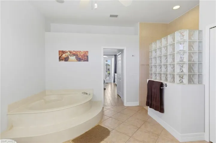 This bathroom features an inviting corner tub, tiled flooring, and a decorative glass block wall