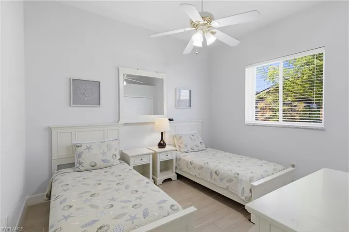 This bright room features light-colored walls and flooring, a ceiling fan, and a window with horizontal blinds providing views of greenery