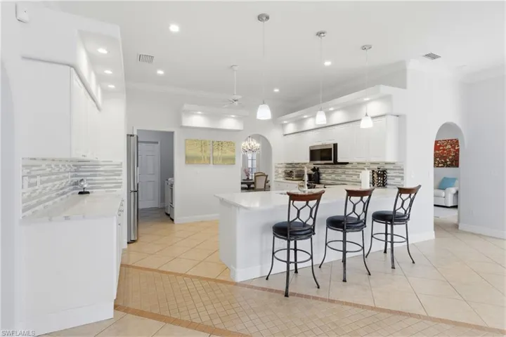 Modern kitchen featuring white cabinetry, stainless steel appliances, a breakfast bar with pendant lighting, and tile flooring