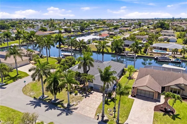 The property is located on a canal with boat docks and features a paved driveway, a well-maintained lawn, and mature palm trees