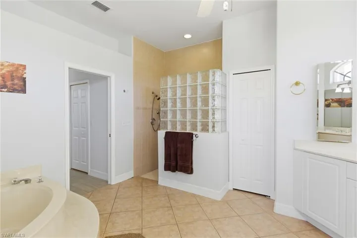 Spacious bathroom featuring a built-in bathtub, a walk-in shower with glass block wall, and vanity with a mirror