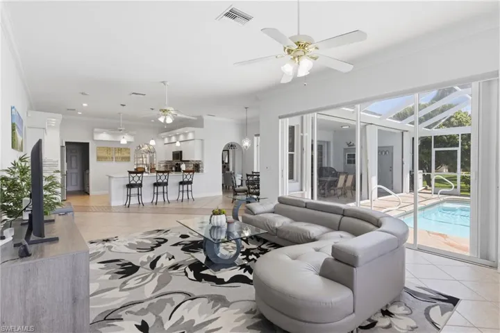 The property offers an open-plan living area with tile flooring, a ceiling fan, and large sliding glass doors providing access to the screened-in patio and pool area