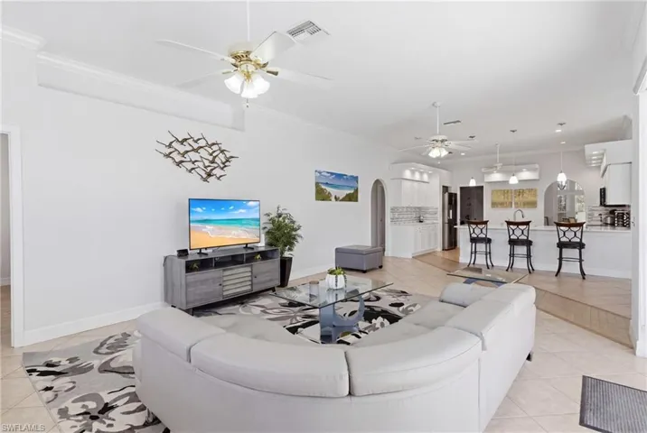 The spacious living area features high ceilings, recessed lighting, and ceiling fans, with an open layout that incorporates a kitchen with a breakfast bar