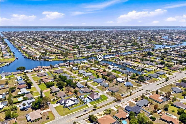 Aerial view of the residential area, featuring a network of canals, a large body of water in the background, and numerous properties with green lawns