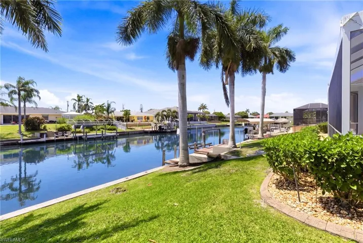 The property features a well-maintained lawn and mature palm trees, with a view of a canal with boat docks