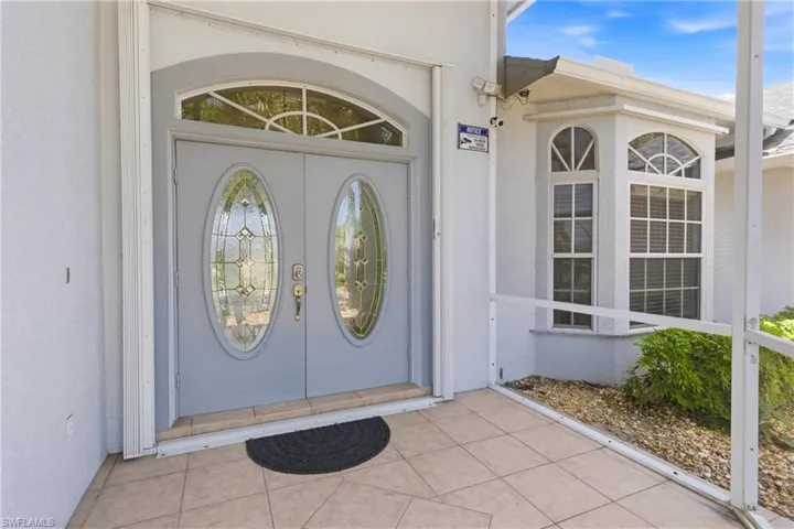 Entryway featuring double doors with decorative glass inserts, an arched transom window, and a tiled porch
