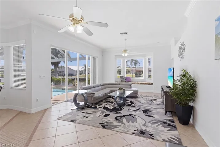 This living area features light-colored tile flooring, white walls, and crown molding