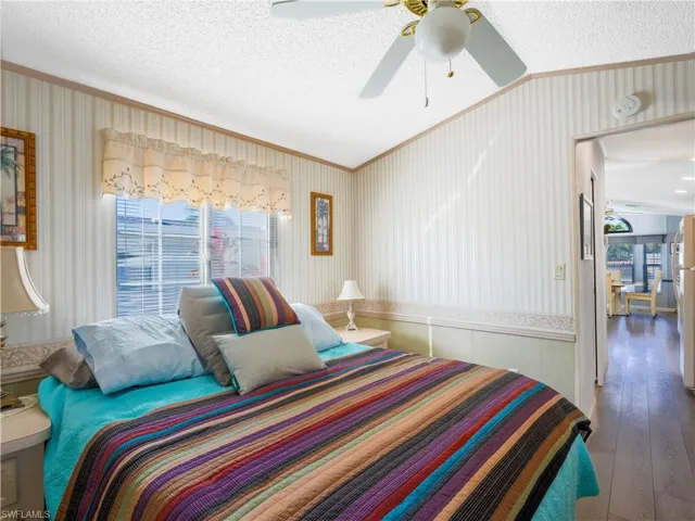 Bedroom featuring a textured ceiling, wallpapered walls, ornamental molding, hardwood / wood-style floors, and a ceiling fan