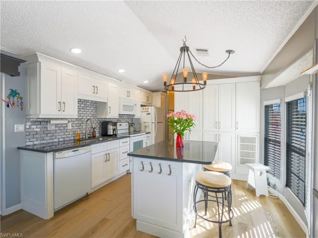 Kitchen featuring a kitchen bar, white appliances, a kitchen island, a textured ceiling, and lofted ceiling