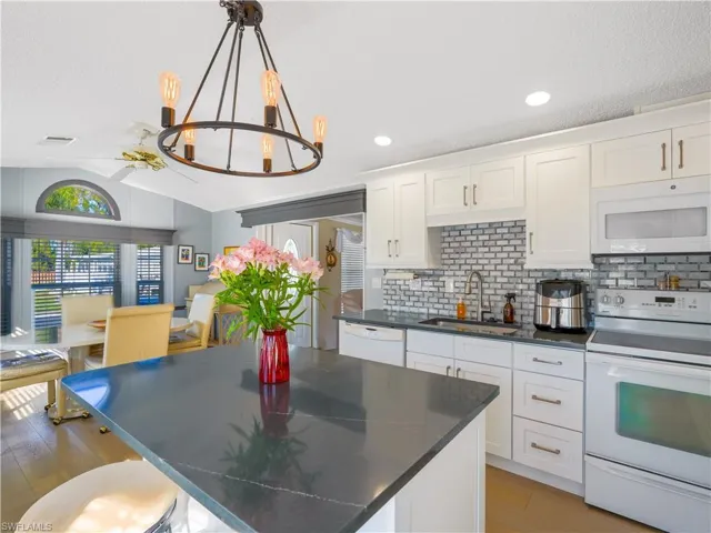 Kitchen featuring white appliances, lofted ceiling, a chandelier, white cabinetry, and a textured ceiling