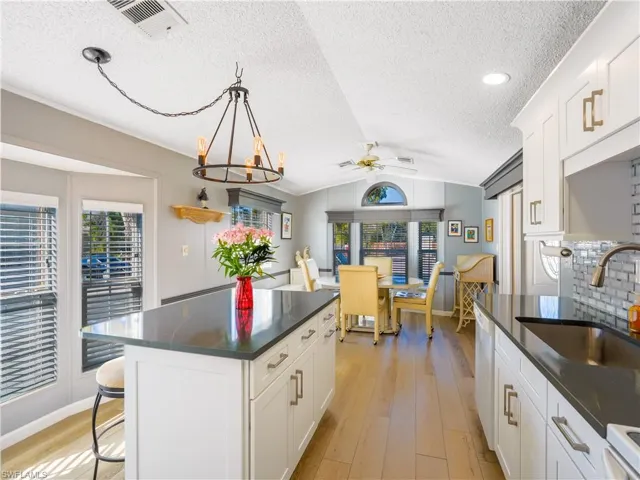 Kitchen with white cabinetry, a breakfast bar area, lofted ceiling, decorative light fixtures, and a center island