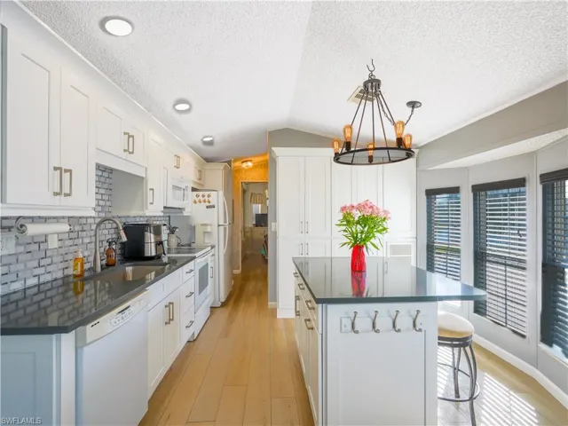 Kitchen featuring white appliances, a kitchen breakfast bar, hanging light fixtures, white cabinetry, and vaulted ceiling