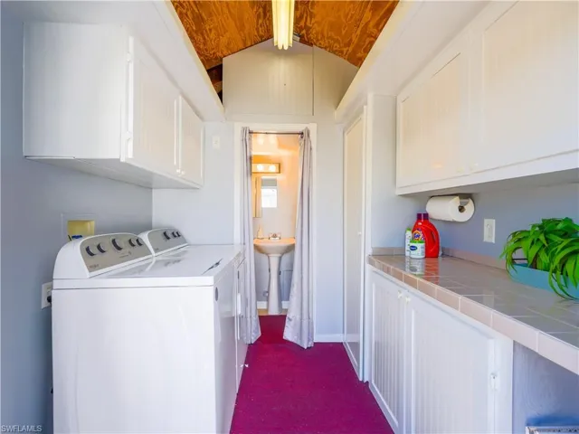 Laundry room with cabinet space, washer and clothes dryer, lofted ceiling, and dark colored carpet