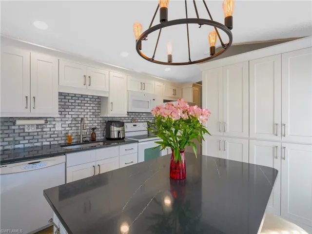 Kitchen featuring white appliances, white cabinetry, tasteful backsplash, a chandelier, and recessed lighting