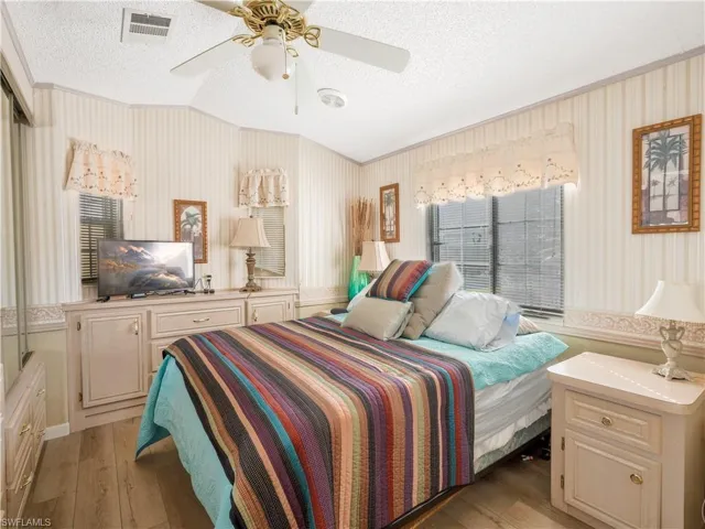 Bedroom with a textured ceiling, light wood finished floors, ceiling fan, lofted ceiling, and wallpapered walls