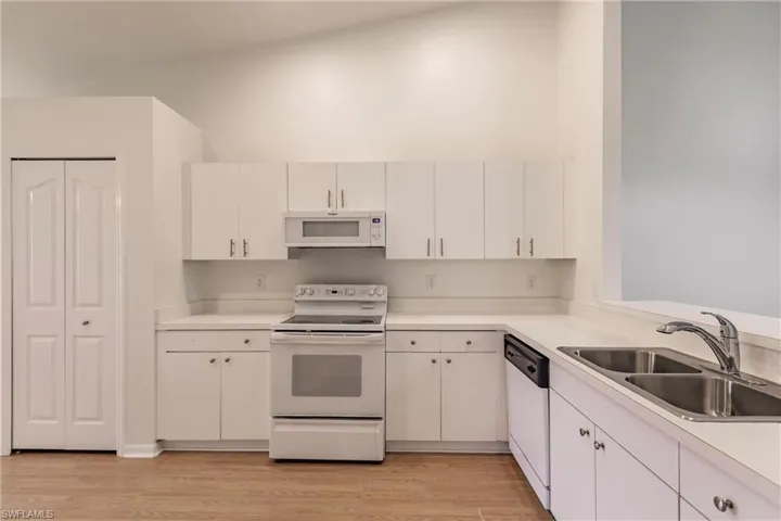Kitchen featuring lofted ceiling, light wood-type flooring, white appliances, white cabinets, and sink