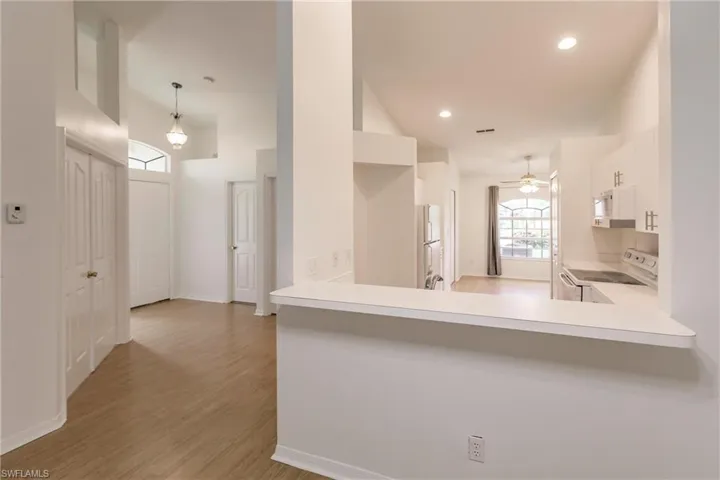 Kitchen with white cabinetry, light wood-type flooring, white appliances, decorative light fixtures, and ceiling fan