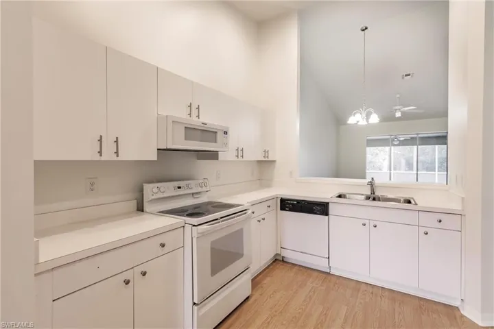 Kitchen with white appliances, light wood-type flooring, pendant lighting, sink, and lofted ceiling