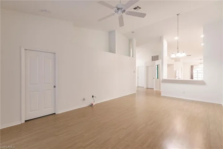 Unfurnished room featuring high vaulted ceiling, ceiling fan with notable chandelier, and hardwood / wood-style flooring