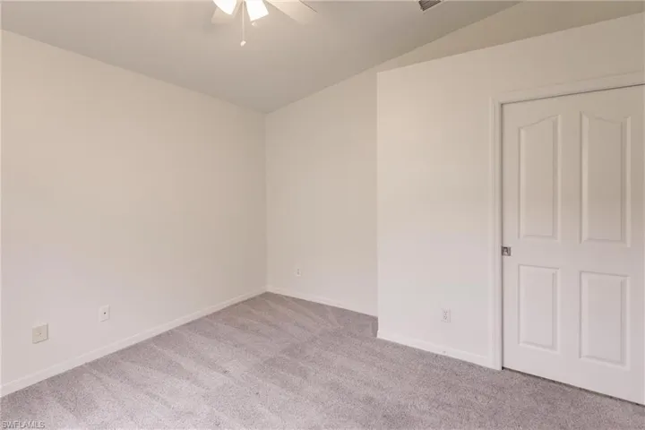 Carpeted empty room featuring vaulted ceiling and ceiling fan