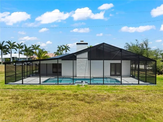 Rear view of property featuring a yard, glass enclosure, an outdoor pool, and a sunroom