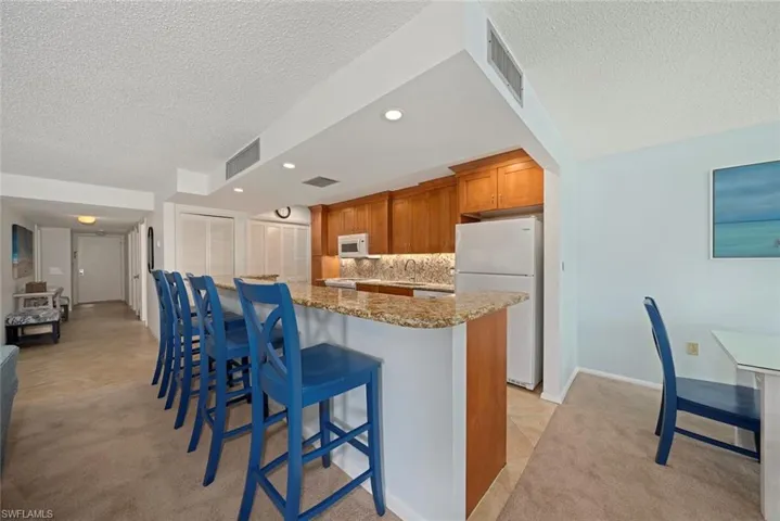 Kitchen with brown cabinets, a breakfast bar area, light carpet, white appliances, and light stone counters