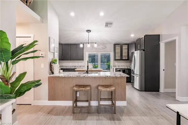 Kitchen with freestanding refrigerator, a peninsula, light stone countertops, light wood-style flooring, and recessed lighting