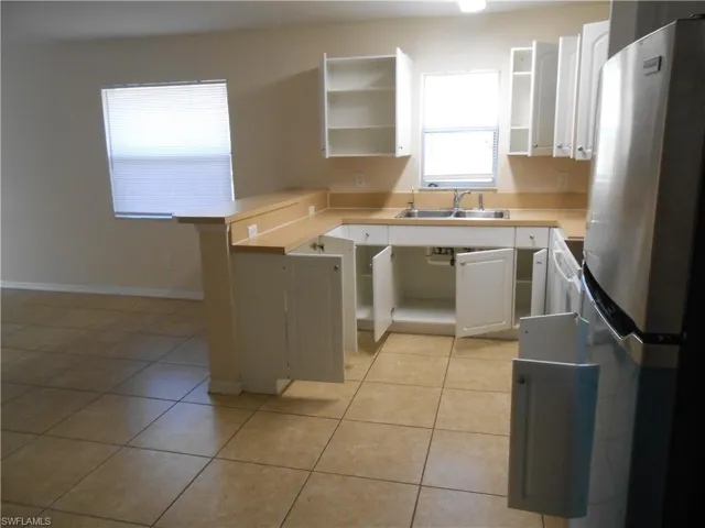 Kitchen featuring freestanding refrigerator, white cabinets, light countertops, and a peninsula