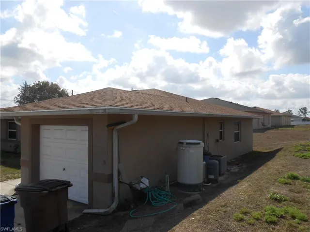 View of side of property featuring a shingled roof, a garage, and stucco siding