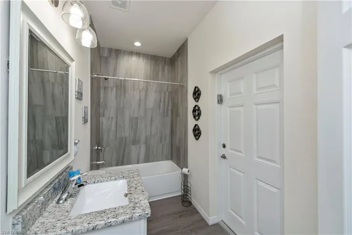 Bathroom featuring vanity, wood finished floors, washtub / shower combination, and recessed lighting