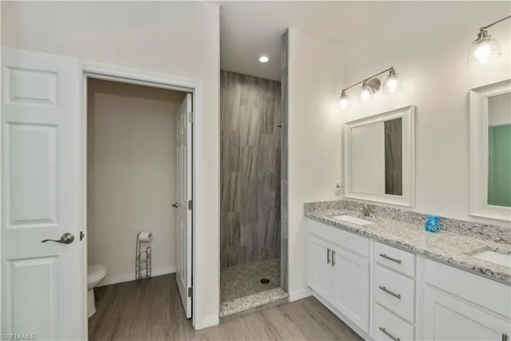 Bathroom featuring double vanity, tiled shower, wood finished floors, and recessed lighting