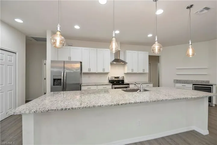 Kitchen with stainless steel appliances, wood finished floors, wine cooler, a large island with sink, and white cabinets